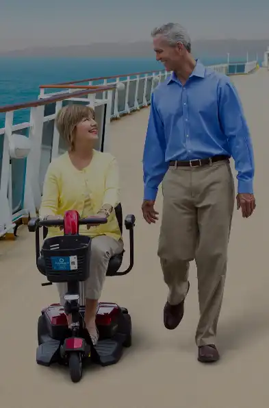 Senior couple walking on a wide cruise ship deck, woman in mobility scooter.